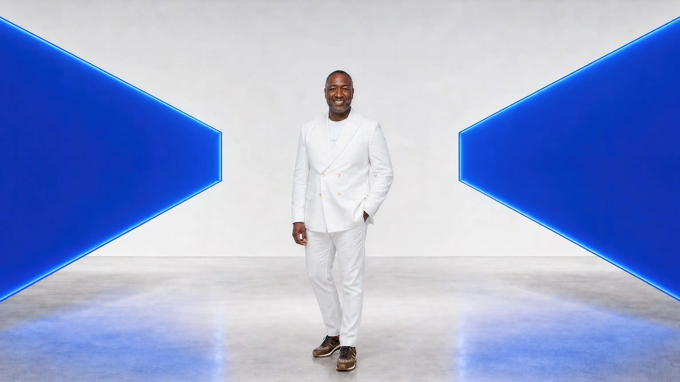 Paul Williams in a cream suit, framed by two illuminated blue perspective panels.
